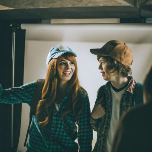 Animated scene featuring Wendy Corduroy and Dipper Pines from Gravity Falls. Wendy has long reddish-brown hair and a warm smile, wearing a plaid green-checkered shirt and blue baseball cap. Dipper, with his signature beanie and playful expression, stands beside her. The backdrop is a simple white canvas.