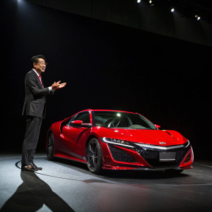 Takahiro Hachigo, CEO of Honda, presenting the new NSX supercar. Dark room, spotlight on car. Red NSX with sleek design.
