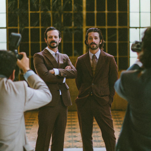 Scoot McNairy and Diego Luna posing for photographers. They are wearing suits. Prominent 'Narcos: Mexico' Season 2 backdrop behind them.