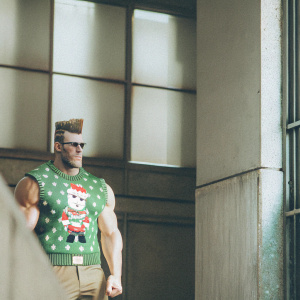 Pixel art sprite of a strong, muscular male character from a video game. Green Family Man shirt with Christmas design. Spiky hair and confident pose. Gray backdrop.