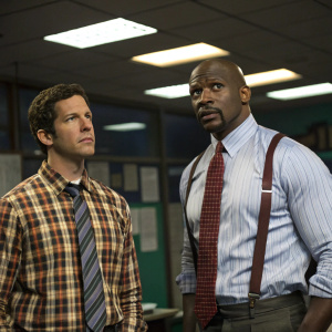 Andy Samberg and Terry Crews at the office. Andy in a plaid shirt and tie, Terry in a striped shirt and bold tie. Background: A dimly lit room with scattered papers and fluorescent lights.