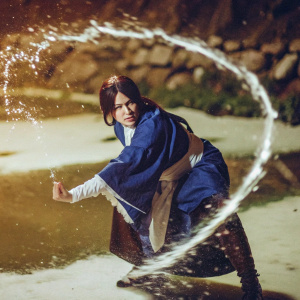 Katara, the waterbender from Avatar: The Last Airbender, standing in a fierce pose. Her blue robes flutter. Water droplets surround her. Dimly lit, snowy landscape