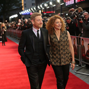 Kenneth Branagh and Alex Kingston attend the premiere of a film. Kenneth Branagh in a black suit, Alex Kingston in a patterned vest. Red carpet event, flashing cameras