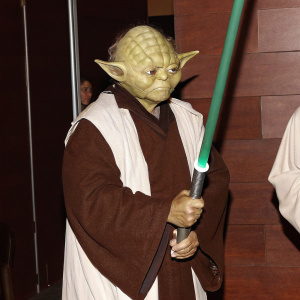 Master Yoda, wielding a green lightsaber. Dark background highlights every detail of his wrinkled skin and intricate robe texture.