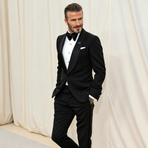 David Beckham in an elegant black tuxedo. Standing against a plain white backdrop. At the Met Gala.