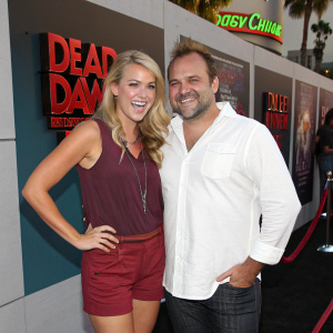 Beckie King and David Deluise at the Dead Before Dawn 3D premiere. Hollywood Blvd. Beckie in maroon top and shorts, David in white shirt. Both with joyful expressions, playful backdrop