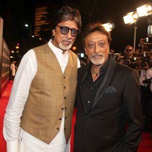 Amitabh Bachchan and Jackie Shroff, iconic film stars, at the Filmfare Awards. Bachchan in white shirt, brown vest. Shroff in black blazer. Red carpet event with flashing cameras