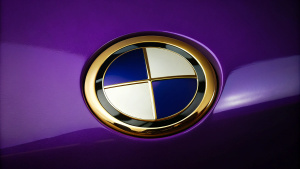 Create a BMW emblem in high-gloss real gold. The emblem lies on an elegant dark purple background without an edge.