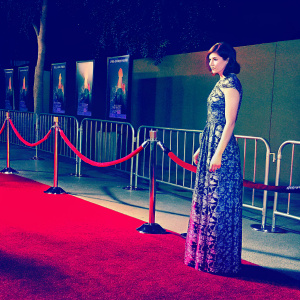 Alexandra Daddario at the Hollywood premiere of 'Percy Jackson: Sea of Monsters'. Dressed in a blue and patterned gown, standing confidently on the red carpet with movie posters and barricades in the background.