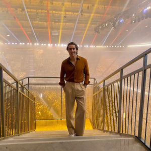 Kendall Schmidt at the Kids' Choice Awards. Caucasian male, stylish brown shirt, beige trousers, friendly pose. Indoor venue, colorful lights, excited crowd.