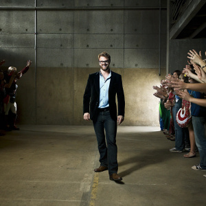 Chris Evans attending the San Diego Comic-Con in a black blazer, light blue shirt, and brown loafers. Surrounded by excited fans and cosplayers.