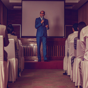 Tharman Shanmugaratnam, chairman of Monetary Authority of Singapore, delivers a speech at a high-profile economic summit. He is wearing a blue suit and glasses. The audience is seated in a modern auditorium.