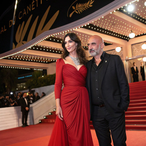 Monica Bellucci and Gaspar Noé at Cannes Film Festival. She wears a stunning red dress, he is bald and in dark attire.