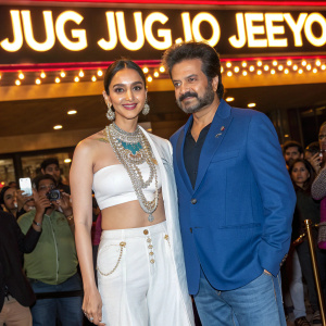 Promotional event for the film 'Jug Jug Jeeyo'. Kiara Advani in white top with intricate jewelry, Anil Kapoor in blue jeans, Varun Dhawan in a blue blazer. Bright lights, fans gathered.