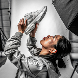Asian woman, serious look, inspecting a Nike Air Max sneaker. Studio backdrop, minimalist