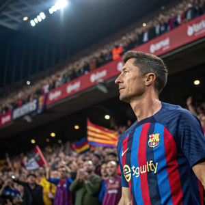 Robert Lewandowski, dressed in a customized blue and red jersey sponsored by Spotify, stands on the sidelines of a crowded stadium. Serious expression, surrounded by fans and team members.