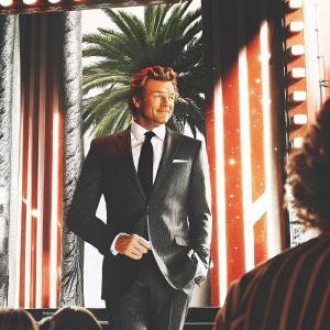 Simon Baker, in a stylish dark suit and tie, at the Hollywood event. He stands confidently in front of a vibrant stage backdrop.