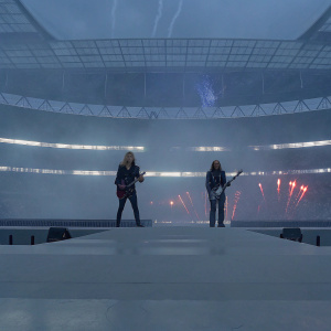 Richie Faulkner and Rob Halford of Judas Priest performing at Wembley Stadium. Crowd and pyrotechnics visible in the background.