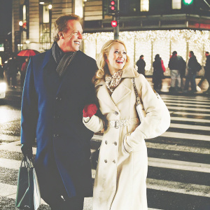 Lee Majors and Faith Majors, beaming with happiness, in the bustling city nightlife. Lee in a dark blue overcoat, their faces illuminated with joy.