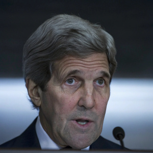 John Kerry, distinguished statesman, intense gaze. Grey hair. Formal attire. Speaking at UN conference. Dark background.