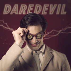 Promotional poster for Netflix series 'Daredevil'. Matt Murdock in a stylish suit with unique dark-rimmed glasses. The glasses feature a distinctive emblem on the lenses. Against a vibrant red backdrop with dynamic, scattered electrical bolts.