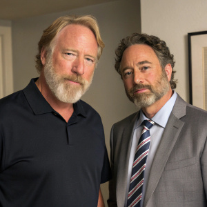 Timothy Busfield, bearded, and David Norona, dressed formally, in the studio set of Lipstick Jungle. Timothy in dark polo shirt, David in gray suit with striped tie. Both focused on the camera in an indoor setting with a neutral wall backdrop.