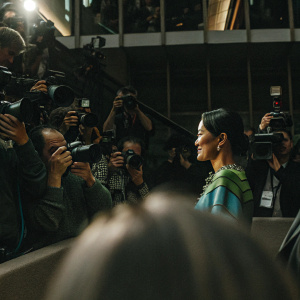 Anne Keothavong, Asian tennis player, at Wimbledon press conference. Wearing a vibrant blue and green blouse, slight smile. Crowded press room with journalists and photographers