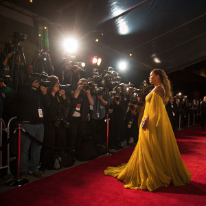 Beyoncé at MTV Movie Awards, dressed in a vibrant, flowing golden gown. Intense spotlight, sea of flashing cameras. High-profile event, red carpet ambiance.