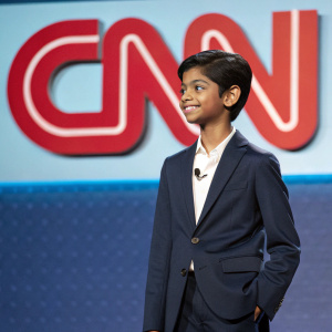 Rohan Chand, a young boy from India, wearing a navy suit and a white shirt, stands confidently at a news conference. The backdrop features the CNN logo in bold letters.