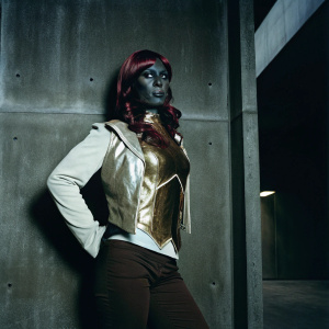 Irelia from League of Legends, an extraterrestrial being with dark skin and fiery red hair. Detailed full-body portrait. Set against a pitch-black backdrop.