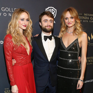 Formal attire of Daniel Radcliffe, Juno Temple, and Heather Graham at a glamorous event. Daniel Radcliffe, bearded, stands center stage. Juno Temple, with long blonde hair, poses on the left. Heather Graham, wearing loose blonde waves, graces the right side. Dark backdrop with event logos