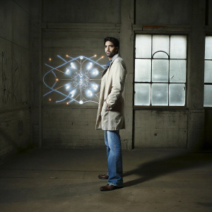 Abhishek Bachchan, standing on a dimly lit stage. Behind him, a dazzling backdrop of vibrant, magical patterns and glowing lights.