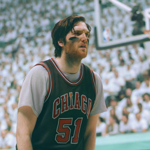 Ryan Arcidiacono in a Chicago Bulls jersey, number 51 visible. Grim determination on his face. The photo, taken at a basketball game, shows a sea of spectators blurred in the background.