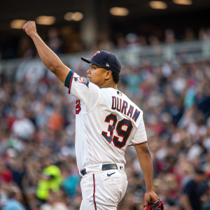 Jhoan Duran of the Minnesota Twins, in white jersey with his name and number, raising his fist after a game. Crowd blurred in the background.