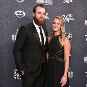 Ryan O'Reilly and Dayna Douros attending the NHL Awards in Las Vegas. He is in a classic black suit, she wears a black dress with unique design. Dark backdrop with NHL logos and text