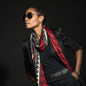 Jada Pinkett-Smith, stylish in sunglasses and a bold scarf, striking a confident pose. Dark studio setting