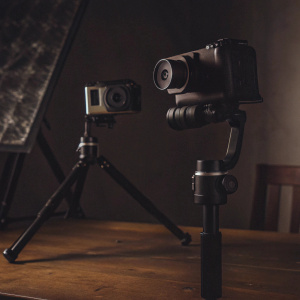 Feiyu Tech FY-G4S gimbal setup. GoPro cameras attached, sleek black design. On a tripod mount in a spacious studio