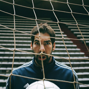 Nikola Karabatic, handball player, intense focus. Wearing a blue adidas jacket. Stadium seats visible in the background.