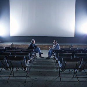 Menahem Golan and Yoram Globus, sitting on director chairs in an empty, dimly lit movie theater.