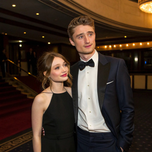 Emily Browning and Max Irons attending the premiere of their new film. Both dressed in formal attire. Emily in a black dress, Max in a black bow tie. The scene is set in a luxurious theater lobby with dim lighting.