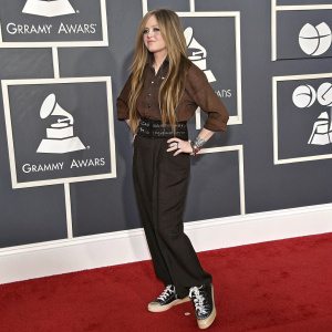 Avril Lavigne at the Grammy Awards, wearing a brown shirt and black belt. Sneakers on her feet. Long brown hair. Backdrop features Grammy logos