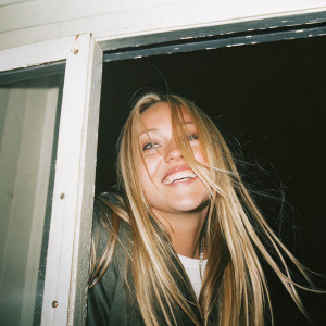 Close-up portrait of Amanda Bynes, grinning widely, with flowing blonde hair. Black backdrop