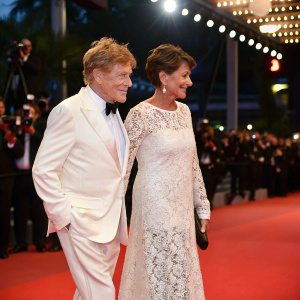 Robert Redford and Sibylle Szaggars on the Cannes Film Festival red carpet. He in a crisp white suit, she in a flowing white lace dress.