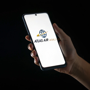 A hand holding a smartphone displaying the Atlas Air Worldwide logo. Black background, high contrast, close-up shot.