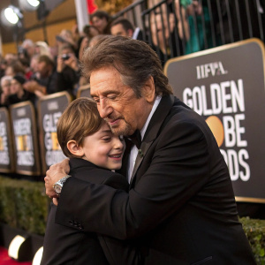 Al Pacino, dressed in a sharp black suit, hugs a young fan at the Golden Globe Awards. Crowds are cheering behind the barriers.