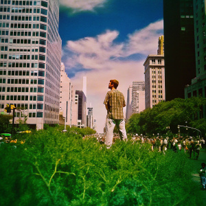 Tobey Maguire in a sea of people, donning a plaid shirt and short hair. Crowded cityscape background.