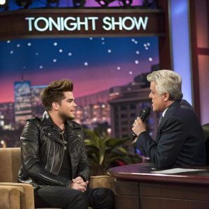 Adam Lambert, wearing a black leather jacket, interviewed by Jay Leno on the Tonight Show stage.