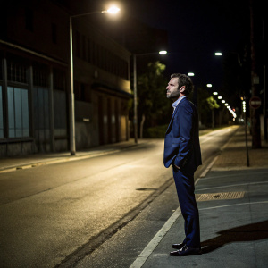 Juan Mata, in a dark blue suit, standing alone on an empty street at night.