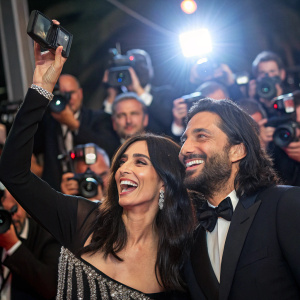Nadine Labaki and Khaled Mouzanar celebrating at the Cannes Film Festival party. The scene is filled with paparazzi flashing their cameras and enthusiastic fans.
