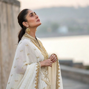 Kareena Kapoor Khan, Indian actress, wearing a white and gold embroidered saree. She stands in a thoughtful pose at a blurred event backdrop.